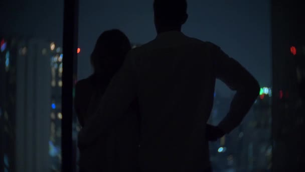 A young couple stands in the background of a panoramic window overlooking the city. Evening night time. 4k, background blur — Stock Video