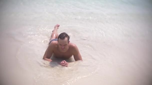 4k, au ralenti, jeune homme couché sur du sable blanc regardant la caméra et souriant — Video