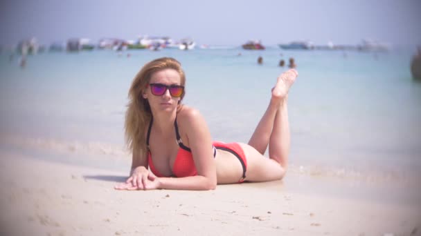 Красивая молодая девушка лежит на пляже в замедленной съемке в красном бикини. тропический отпуск. Почти. 4k — стоковое видео