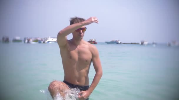 4k, αργή κίνηση, χοροί νεαρού άνδρα στη θάλασσα, με γυαλιά πιτσιλιές νερού και χαμόγελα — Αρχείο Βίντεο