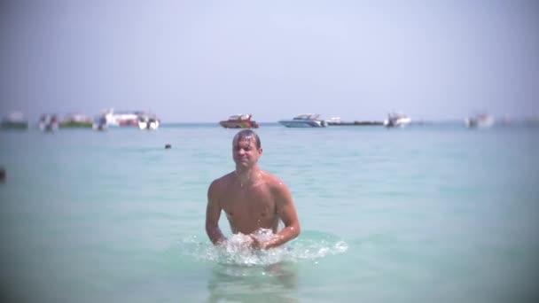4k, αργή κίνηση γυρίσματα, ένας νεαρός άνδρας βουτιές στη θάλασσα φορώντας γυαλιά ηλίου. αναδύεται και χαμόγελα — Αρχείο Βίντεο
