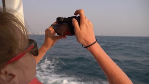 Een mooie vrouw staat op de achtersteven van het schip en maakt een video op de camera. Golven op de achtergrond, slow motion, 4k — Stockvideo