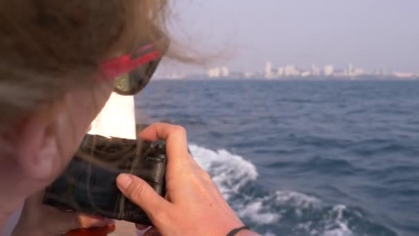 Μια όμορφη γυναίκα στέκεται στην πρύμνη του πλοίου και να κάνει ένα βίντεο για τη φωτογραφική μηχανή. Κύματα στο παρασκήνιο, αργή κίνηση, 4k — Αρχείο Βίντεο