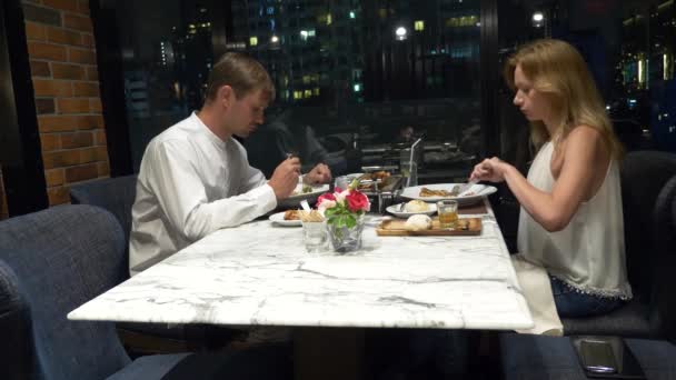 Pareja feliz hablando y cenando en un bar con vistas a los rascacielos, por la noche, 4k, fondo borroso — Vídeo de stock