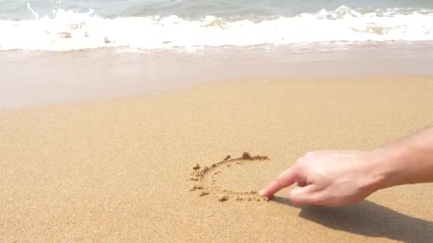 Fala kasuje napisy napisane na piasku. 4k, zwolnionym tempie, widok z góry. malowane sercem — Wideo stockowe