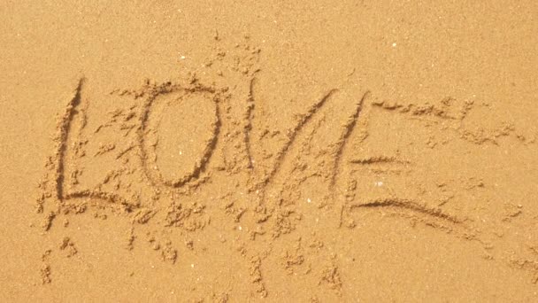 海の波は、砂に書いた銘刻文字を消去します。4 k、スローモーション、平面図です。愛という言葉 — ストック動画