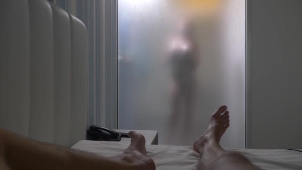 Žena za rozmazaná sklem. Dívka, připravuje si sprchu. Žena v koupelně. muž hodinky, jako žena bere sprchu přes skleněnou stěnu ve sprše. 4k — Stock video