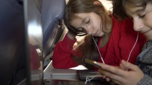 4 k, close-up, kinderen, passagiers in een vliegtuig tegen de patrijspoort de telefoon gebruiken. — Stockvideo