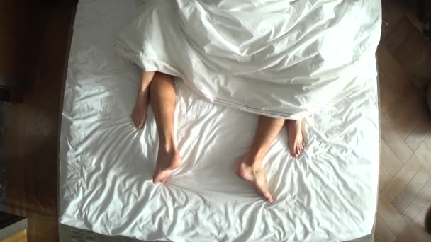 Ένας άνδρας και μια γυναίκα στο κρεβάτι. Ανδρική και γυναικεία πόδια κάτοψη, λευκά είδη — Αρχείο Βίντεο