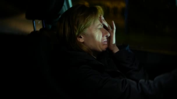 Mujer con chaqueta Se sienta en el coche llorando. noche y lluvia, 4k, desenfoque de fondo — Vídeo de stock