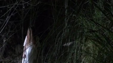 Bir bıçak ve bir yumuşak oyuncak ile ormanda dolaşıp küçük bir hayalet kız beyaz, uzun siyah saçlı. 4k