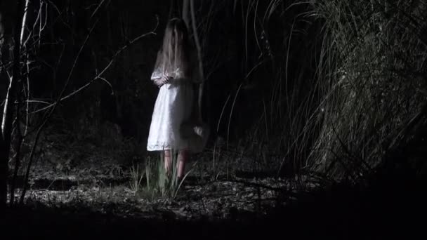 Una niña fantasma con el pelo largo y negro, en blanco, vagando por el bosque con un cuchillo y un juguete suave. 4k — Vídeo de stock