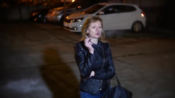 Στοχαστικός, γυναίκα καπνίζει ένα τσιγάρο. στην πόλη το βράδυ, στο πάρκινγκ — Αρχείο Βίντεο