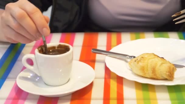 Primer plano de una mano femenina. Una mujer en un restaurante con una bebida caliente y un croissant. un suéter caliente y bufanda , — Vídeos de Stock