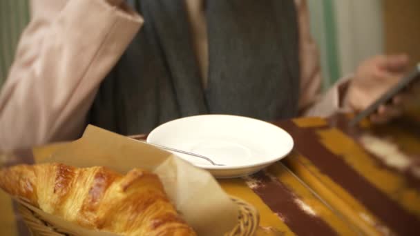 Nahaufnahme einer weiblichen Hand. eine Frau in einem Restaurant mit einem heißen Getränk und einem Croissant. ein warmer Pullover und Schal, 4k. — Stockvideo