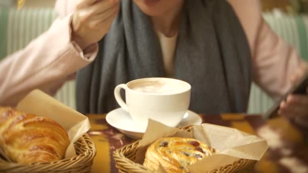 Nahaufnahme einer weiblichen Hand. eine Frau in einem Restaurant mit einem heißen Getränk und einem Croissant. ein warmer Pullover und Schal, 4k. — Stockvideo