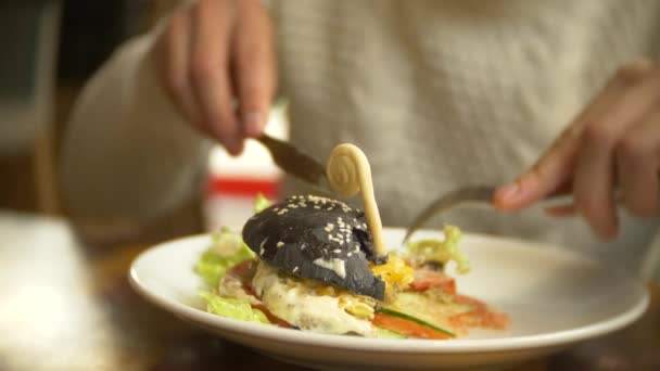 Man in een witte trui een zwarte hamburger eten in een restaurant. 4k — Stockvideo