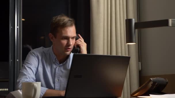 Jeune homme d'affaires parlant au téléphone fixe, assis au bureau la nuit. carnet de notes. 4k — Video