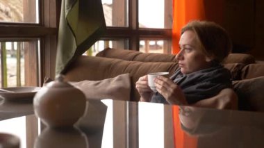 Genç kadın pencere Deniz Manzaralı yakınındaki kafede çay içme. bir kadın bir eşarp ve kazak çay içme ve bir kafede tadını çıkarma. 4k