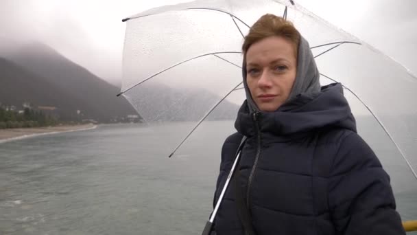 Una mujer bajo un paraguas junto al mar bajo la lluvia, 4k en un día lluvioso de otoño — Vídeos de Stock