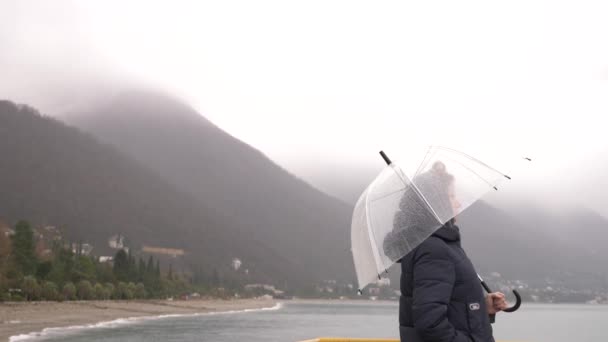 Una mujer bajo un paraguas junto al mar bajo la lluvia, 4k en un día lluvioso de otoño — Vídeos de Stock