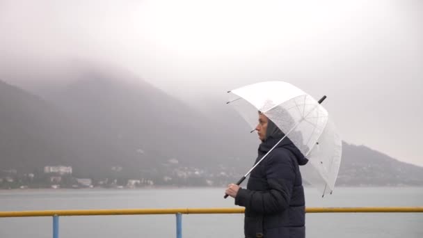 Eine Frau unter einem Regenschirm am Meer im Regen, 4k an einem regnerischen Herbsttag — Stockvideo