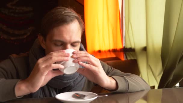 若い男を着てスカーフ飲む紅茶とカフェで笑顔。4 k — ストック動画