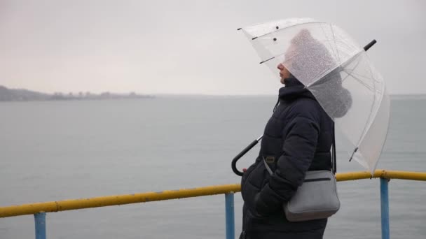 Una mujer bajo un paraguas junto al mar bajo la lluvia, 4k en un día lluvioso de otoño — Vídeo de stock