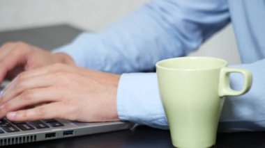 Ofiste çalışırken dizüstü bilgisayarda sipping çay genç adam. yakın çekim, 4k