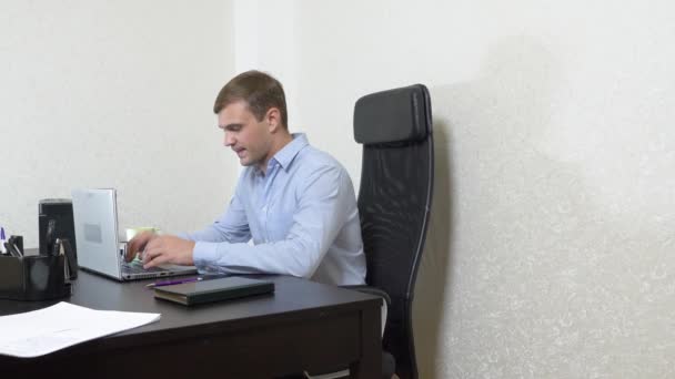 Молодой человек потягивает чай на ноутбуке во время работы в офисе. Съемка замедленного действия, 4k — стоковое видео