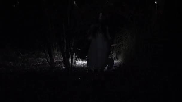 Une petite fille fantôme aux longs cheveux noirs, en blanc, errant dans les bois avec un couteau et un jouet doux. 4k — Video