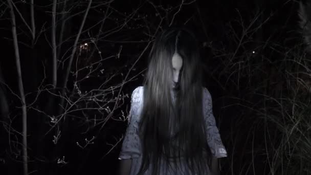En liten ghost flicka med långt svart hår, i vitt, vandra genom skogen med en kniv och en mjuk leksak. 4k — Stockvideo