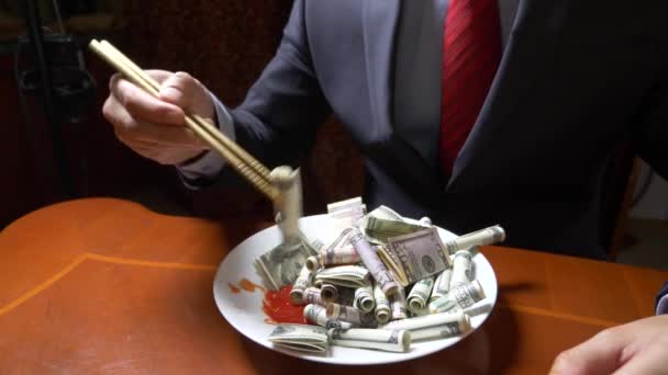 O homem de casaco e gravata está a comer os rolos do dólar com pauzinhos. Comer dólares. 4k . — Vídeo de Stock