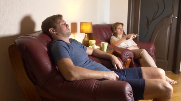 Un cuplu căsătorit stând pe un scaun și uitându-se la televizor acasă împreună. 4k, seara târziu, întuneric . — Videoclip de stoc