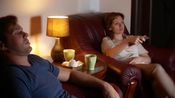 Una pareja casada sentada en una silla y viendo televisión en casa juntos. 4k, tarde en la noche, oscuro . — Vídeo de stock