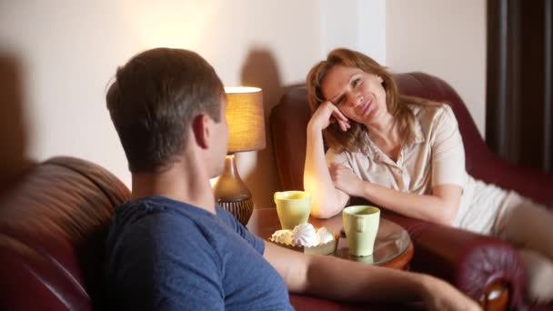 Gelukkig paar man en vrouw zitten thuis in de woonkamer, praten ontspannen en thee drinken 's avonds laat. 4k — Stockvideo
