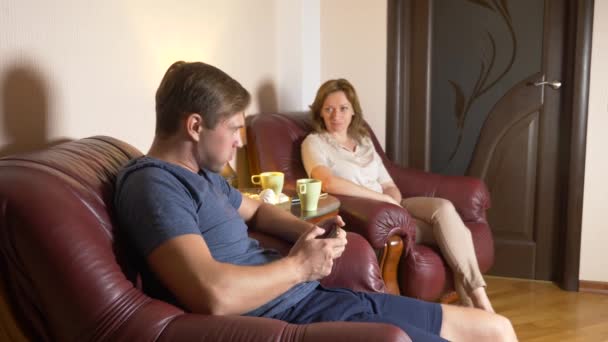 Pareja feliz marido y mujer están sentados en casa en la sala de estar, hablando relajarse y beber té tarde en la noche. 4k — Vídeos de Stock