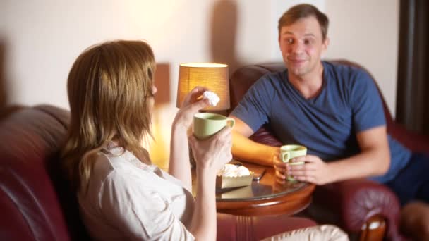 Pareja feliz marido y mujer están sentados en casa en la sala de estar, hablando relajarse y beber té tarde en la noche. 4k — Vídeos de Stock