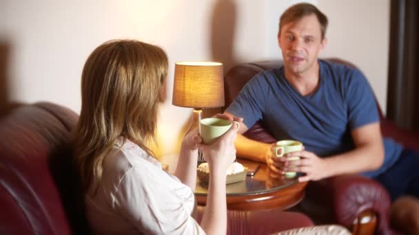 Pareja feliz marido y mujer están sentados en casa en la sala de estar, hablando relajarse y beber té tarde en la noche. 4k — Vídeos de Stock