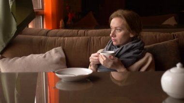 Genç kadın pencere Deniz Manzaralı yakınındaki kafede çay içme. bir kadın bir eşarp ve kazak çay içme ve bir kafede tadını çıkarma. 4k