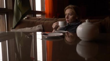 Genç kadın pencere Deniz Manzaralı yakınındaki kafede çay içme. bir kadın bir eşarp ve kazak çay içme ve bir kafede tadını çıkarma. 4k