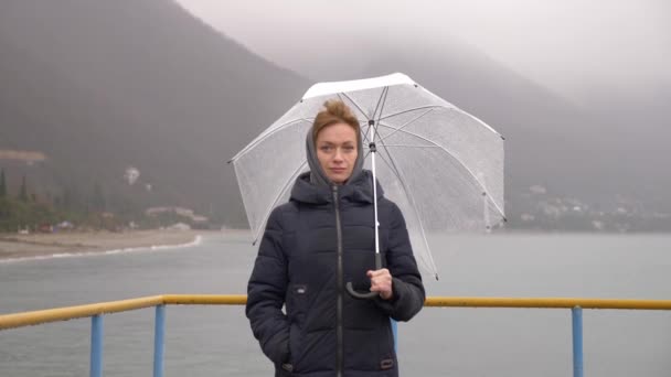 Žena pod slunečníkem u moře v dešti, 4k na deštivé podzimní den — Stock video