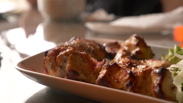 Закрытие жареного мяса, лежащего на белой тарелке с зеленью на столе в замедленной съемке, 4k, пар из горячего мяса — стоковое видео