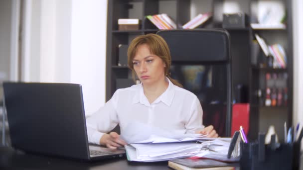 Uma mulher de negócios que digitaliza documentos, franjas, usando um laptop, não executa uma tarefa urgente no escritório, não há tempo suficiente, 4k. o escritório está quente, o ar condicionado não está funcionando — Vídeo de Stock