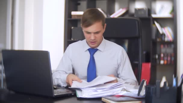 A businessman who scans documents, frowns, using a laptop, does not perform an urgent task in the office, there is not enough time, 4k — Stock Video