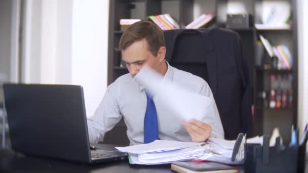 En affärsman som skannar dokument, rynkar pannan, använder en bärbar dator, utför inte en brådskande uppgift på kontoret, det finns inte tillräckligt med tid, 4k. kontoret är varmt, luftkonditioneringen fungerar inte — Stockvideo