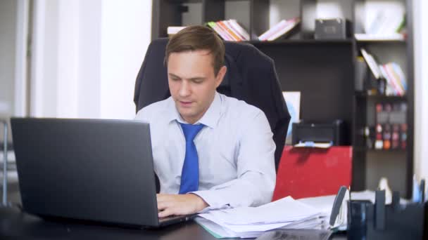 Un homme d'affaires qui scanne des documents, fronce les sourcils, à l'aide d'un ordinateur portable, n'effectue pas une tâche urgente dans le bureau, il n'y a pas assez de temps, 4k. le bureau est chaud, la climatisation ne fonctionne pas — Video