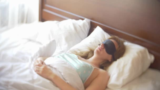 Mujer joven con una máscara para dormir, durmiendo en la cama sobre una almohada durante el día. 4k . — Vídeos de Stock