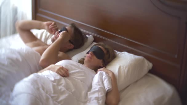 Una mujer casada y un hombre en una máscara para dormir, dormir en la cama en una almohada durante el día. 4k . — Vídeo de stock