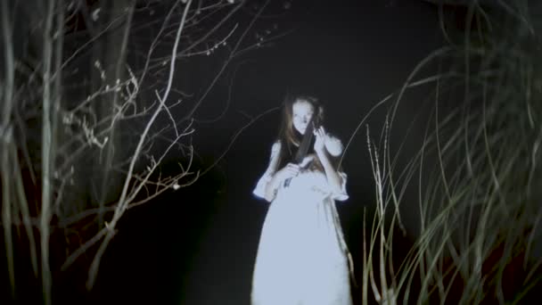 Маленька дівчинка-привид з довгим чорним волоссям, в білому кольорі, блукає лісом з ножем і м'якою іграшкою. 4k — стокове відео